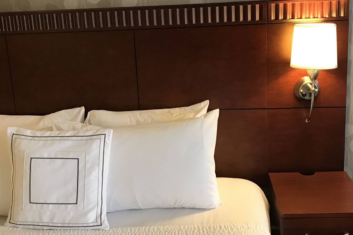 Una camera d'albergo con un letto rifatto, una lampada da comodino e un comodino.