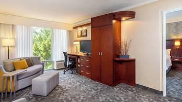 A hotel room with a grey sofa, a wooden desk, a television, and a large window with curtains.