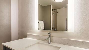 A bathroom with a white speckled countertop, a rectangular sink, a mirror, and a shower with a grab bar.