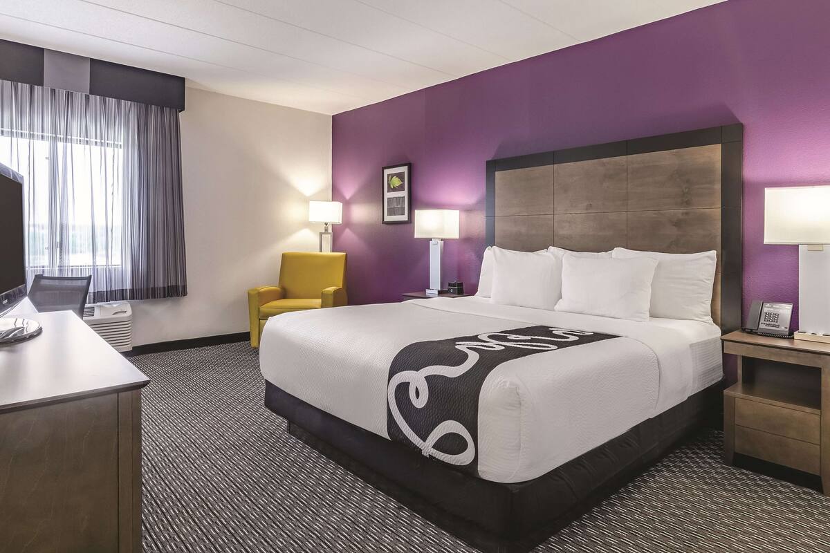A hotel room with a large bed, a desk, a chair, and a TV.
