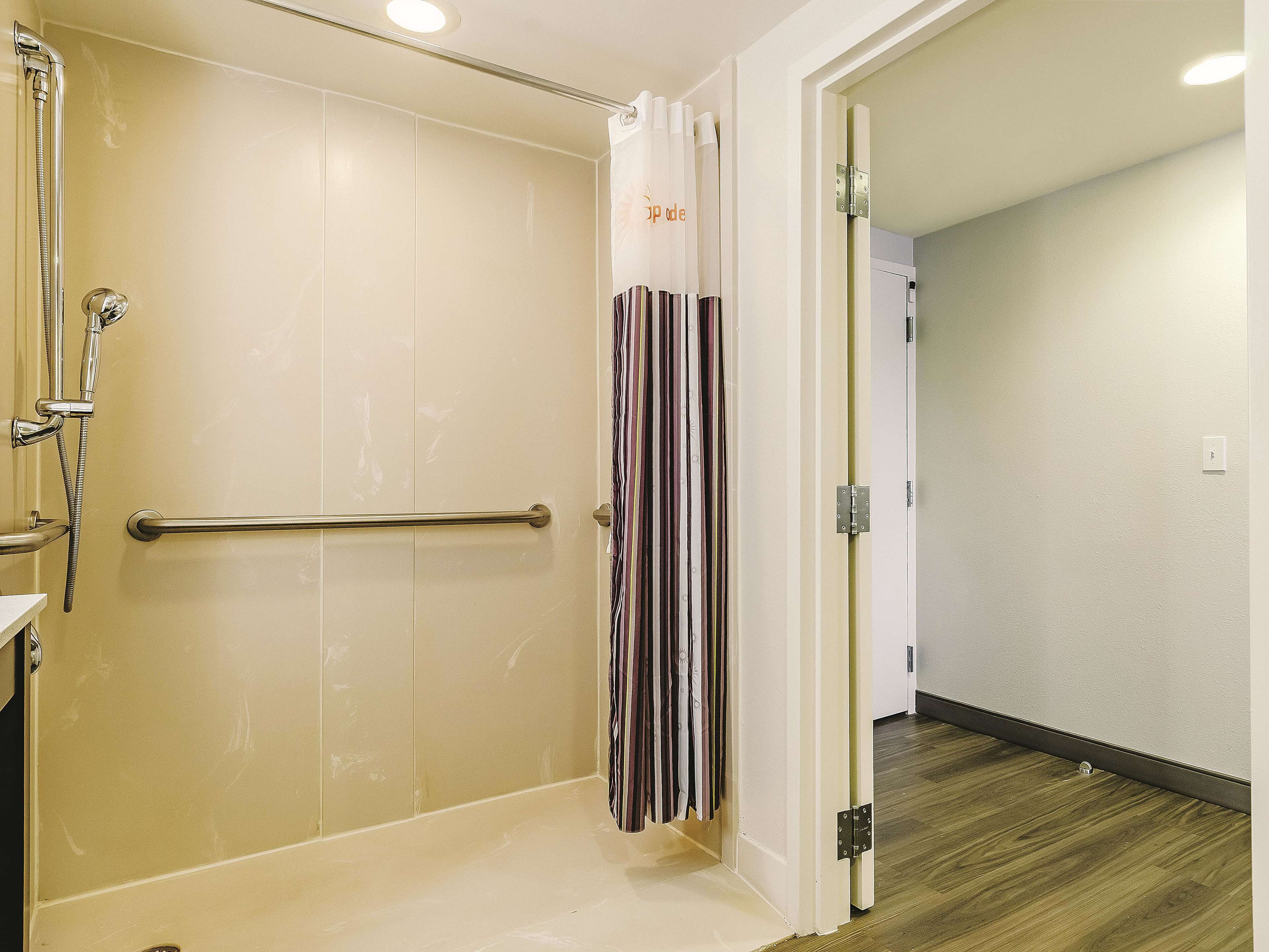 A bathroom with a shower, a handrail, and a striped curtain.