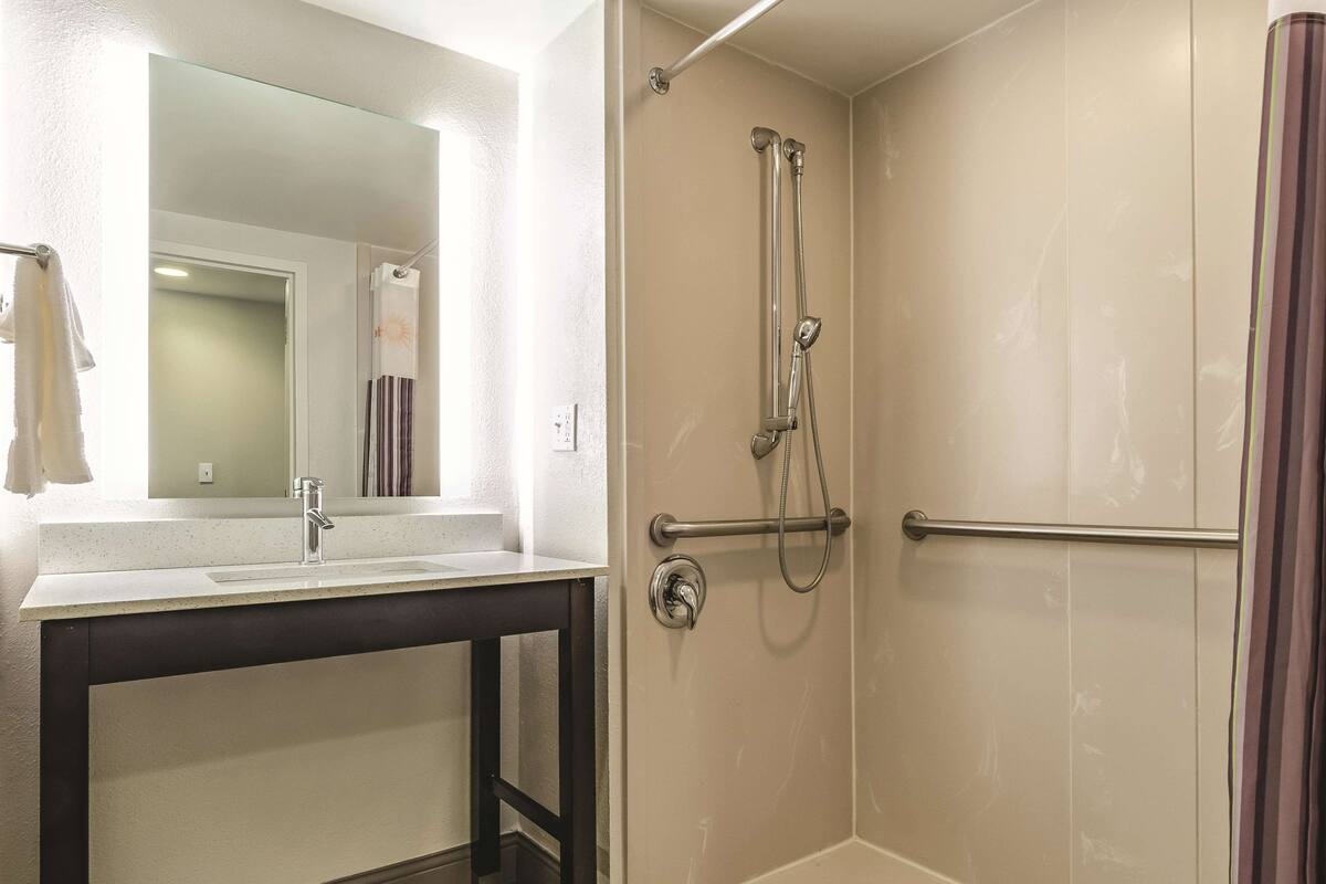 A bathroom with a white sink, a mirror, and a shower with a handrail.