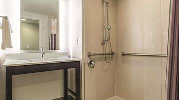 A bathroom with a white sink, a mirror, and a shower with a handrail.