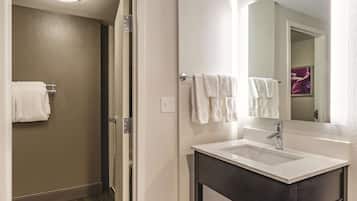 A bathroom with a white sink, dark vanity, and a mirror. There is a towel rack with white towels and a door leading to a shower area.