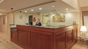 Un comptoir d’accueil avec un réceptionniste, une horloge, une enseigne indiquant « La Quinta » et une lampe.