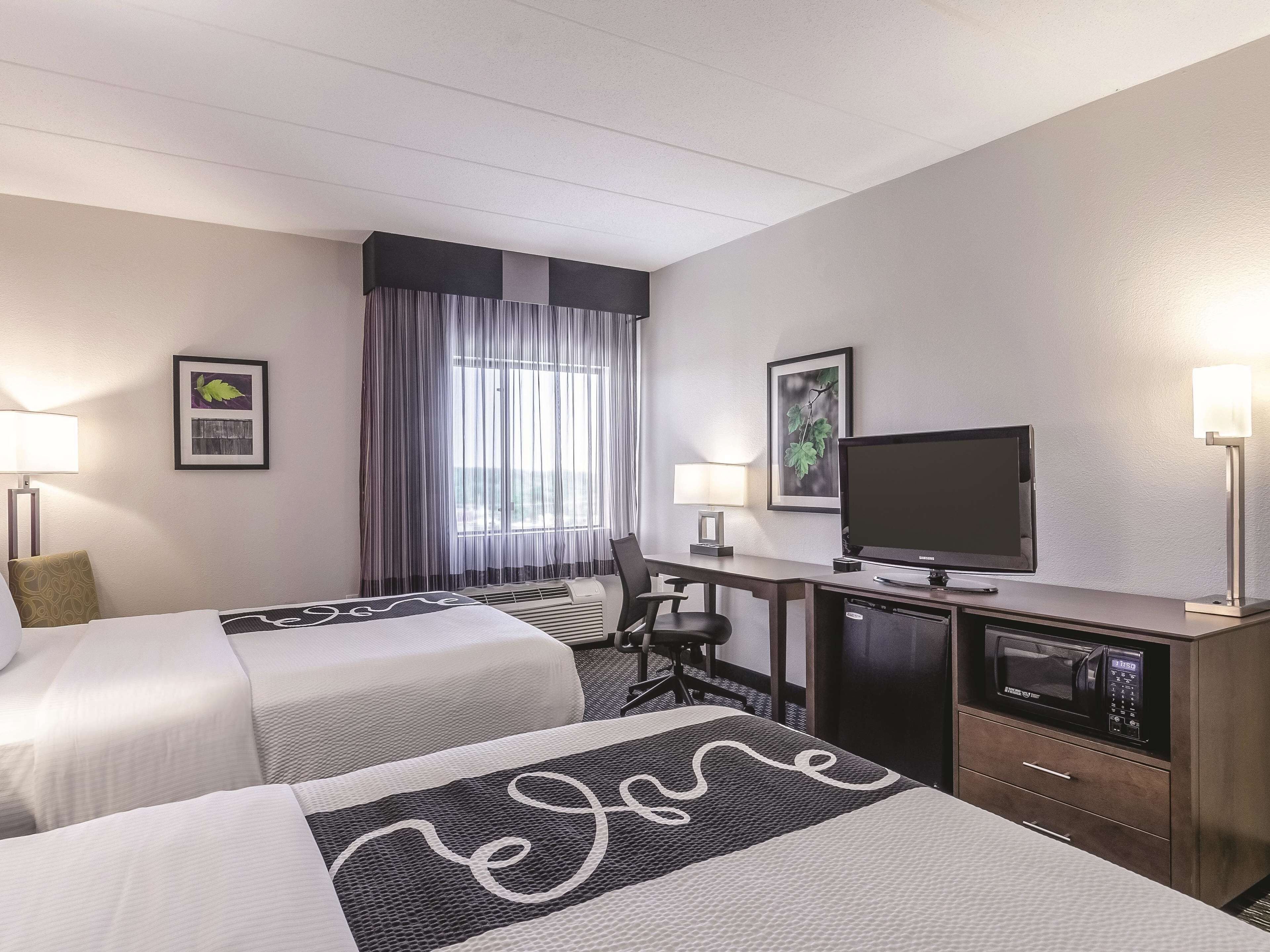 Een hotelkamer met twee bedden, een bureau met een computer, een televisie en een magnetron.