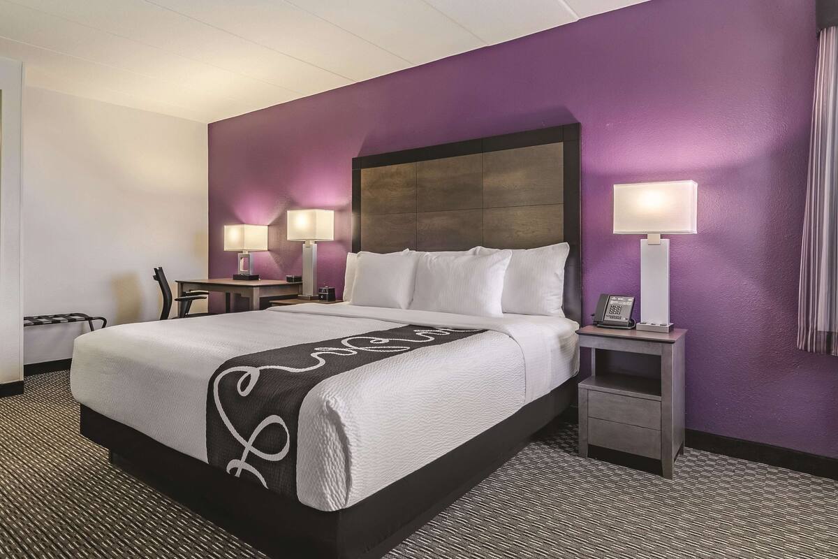 A hotel room with a large bed, two bedside tables with lamps, a chair, and a small table.