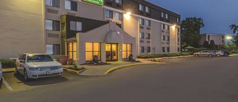 A hotel with a prominent sign, a parking lot, and a well-lit entrance.