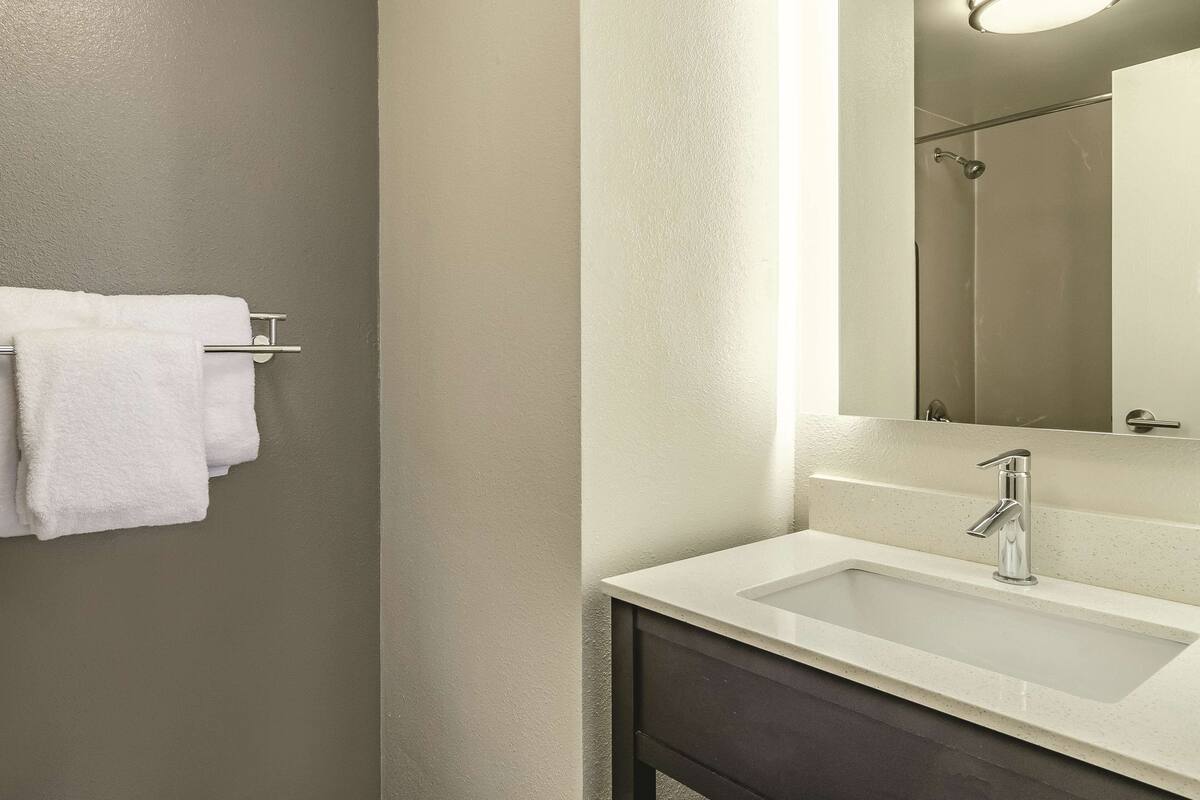 A modern bathroom with a white sink, a mirror, and a towel rack with white towels.