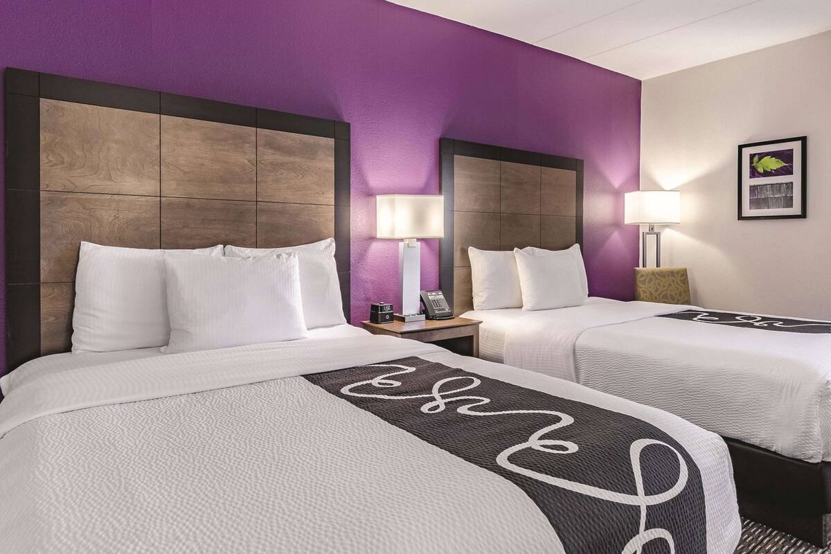 A hotel room with two beds, a purple wall, and a framed picture on the wall.
