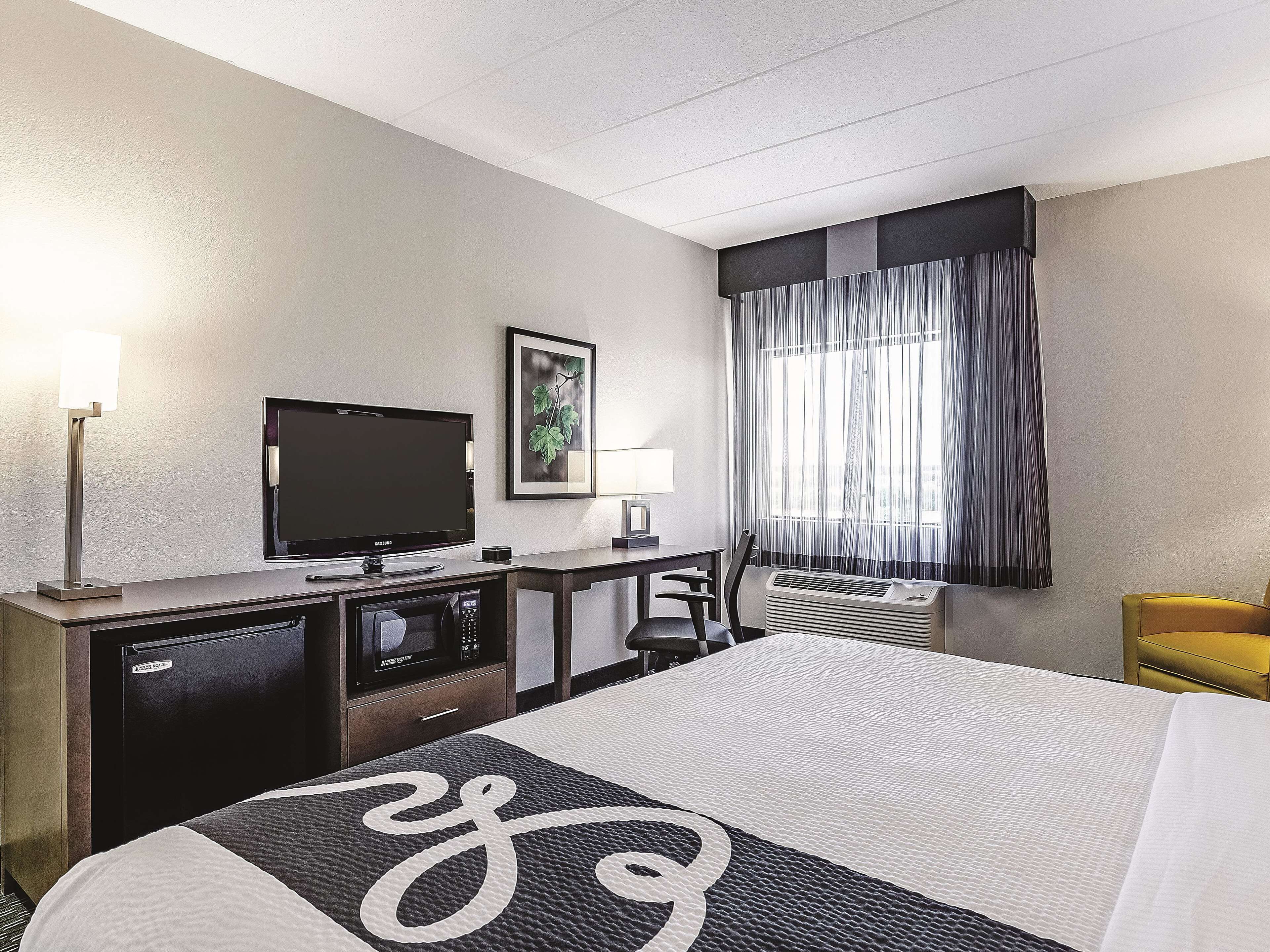 Ein Hotelzimmer mit Bett, Schreibtisch, Fernseher, Mikrowelle und einem Fenster mit Vorhängen.