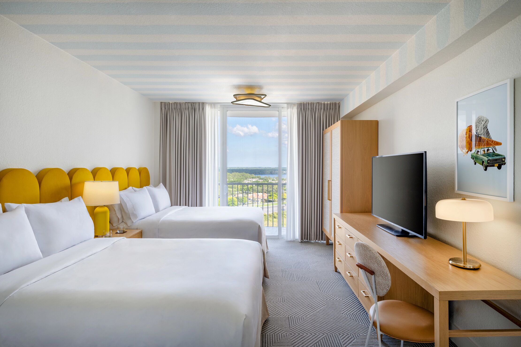 Quarto de hotel com duas camas, televisão, escrivaninha e vista para o exterior.