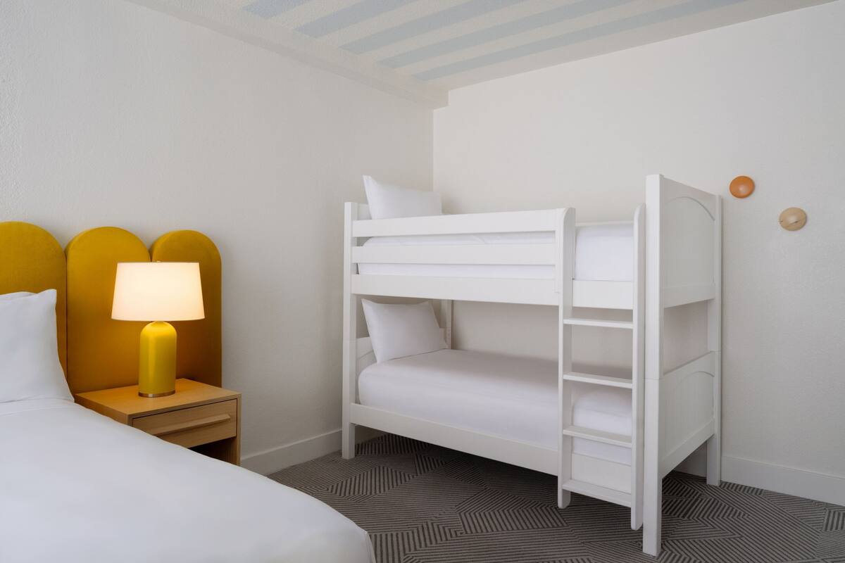 A bunk bed in a hotel room with a nightstand and a lamp.