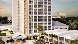 A high-rise hotel with a pool area, including sun loungers and umbrellas, surrounded by palm trees.