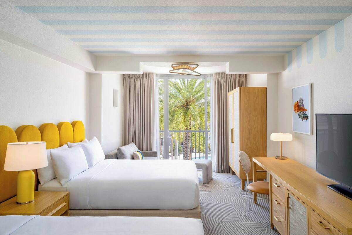 A hotel room with a bed, a desk, a chair, a TV, and a balcony with curtains.
