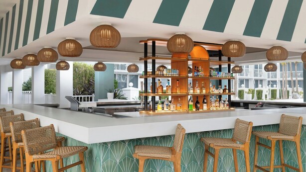 A bar area with wicker chairs, a bar counter, and shelves of bottles.