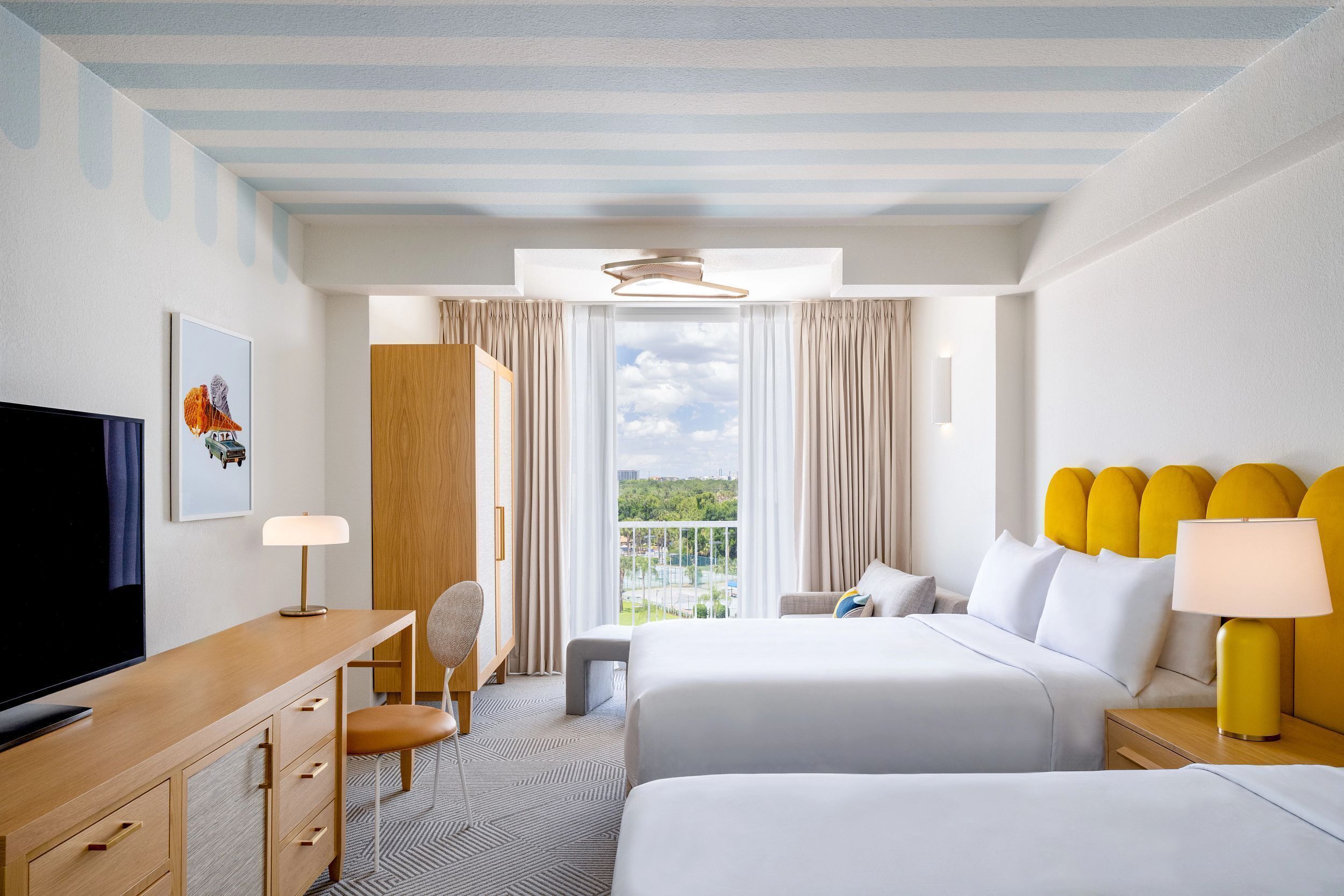 Quarto de hotel com cama, escrivaninha, televisão, cadeira e janela com cortinas.