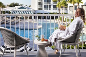 Una persona seduta a un tavolo con vista su una piscina, lettini e un edificio sullo sfondo.