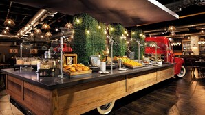 A buffet with various food items, a red food truck, and a green wall with hanging lights.