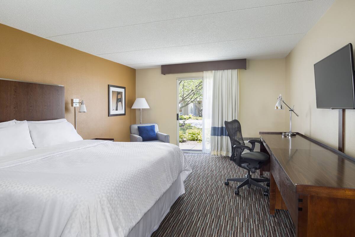 A hotel room with a large bed, a desk with a chair, a television, and a window with curtains.