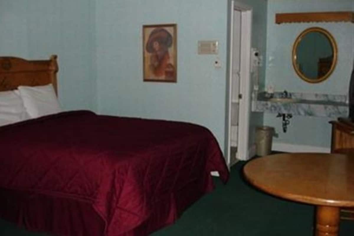 Quarto com uma cama, uma mesa de madeira redonda, um espelho e um quadro na parede.