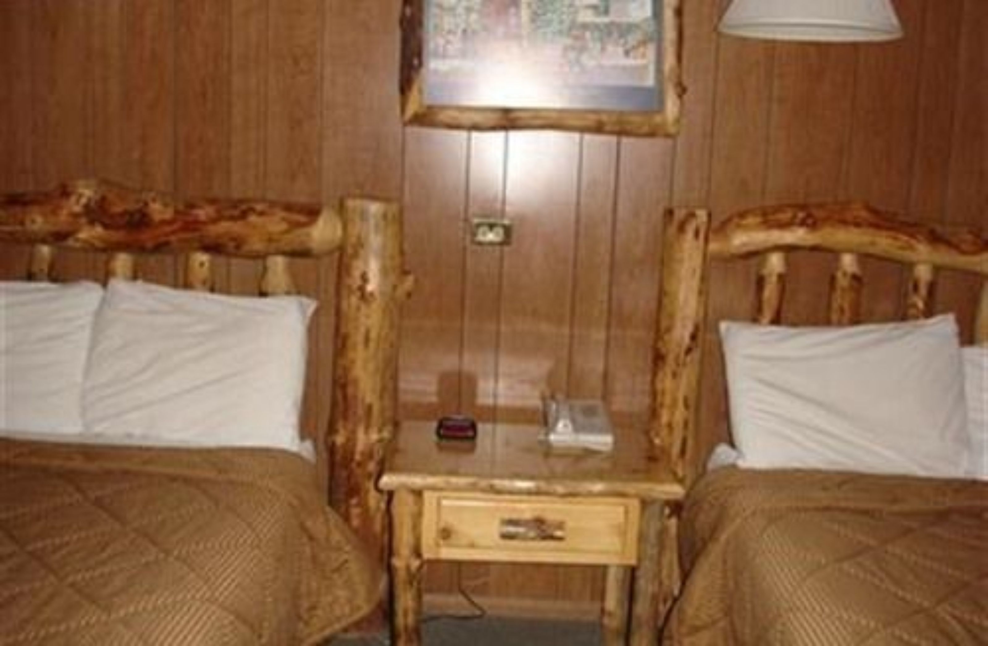 Une pièce en bois avec deux lits, une petite table et une lampe fixée au mur.