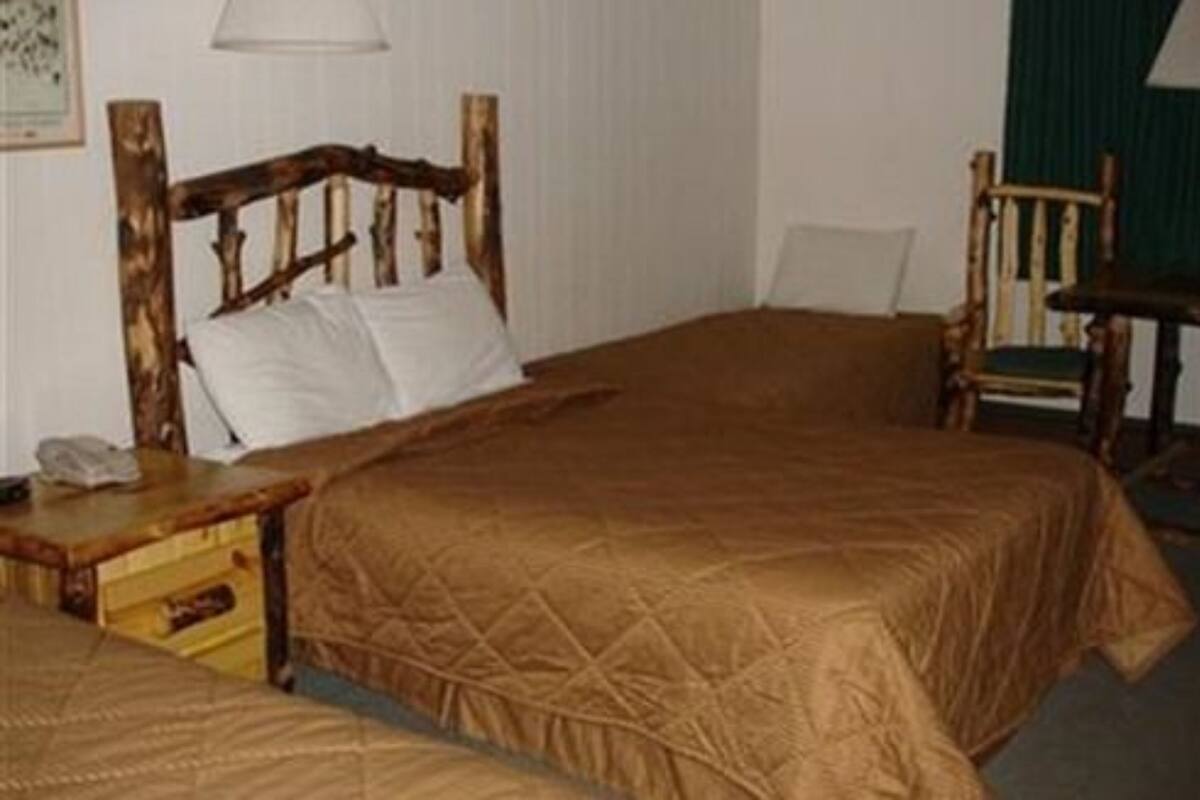 Quarto com cama de madeira, mesa de cabeceira de madeira, uma cadeira e uma pequena mesa.