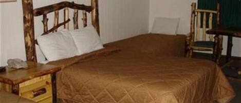 Una habitación con una cama de madera, una mesita de noche de madera, una silla y una pequeña mesa.