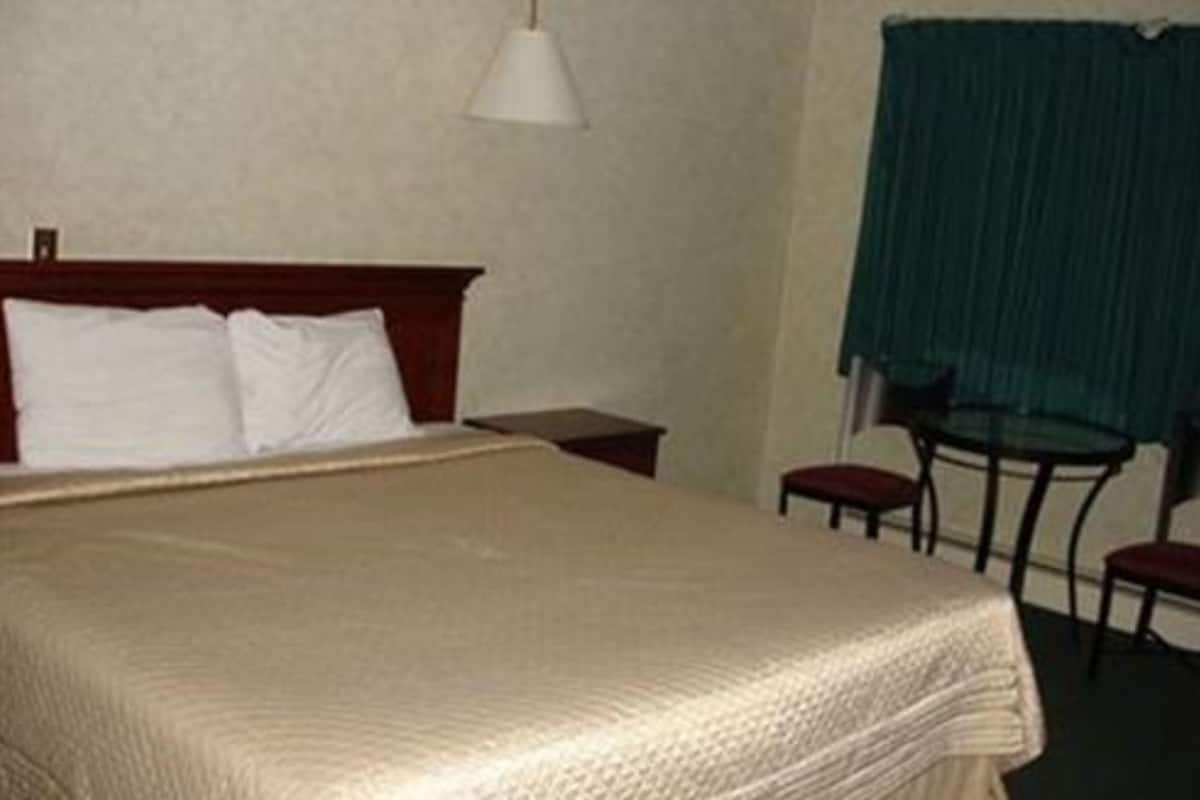 Quarto de hotel com cama, mesa de cabeceira, abajur, cadeira e mesa.