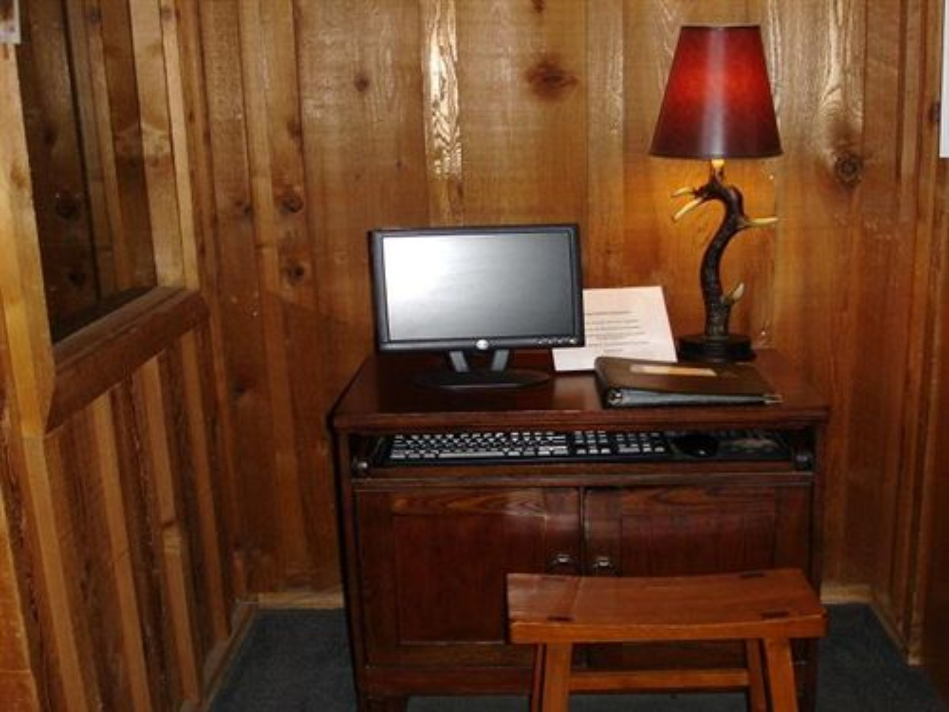 Un escritorio de madera con un monitor de computadora, teclado y una lámpara.