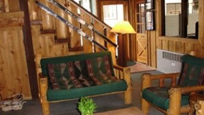 A wooden interior with a sofa, armchairs, a small table with a plant, and a staircase.