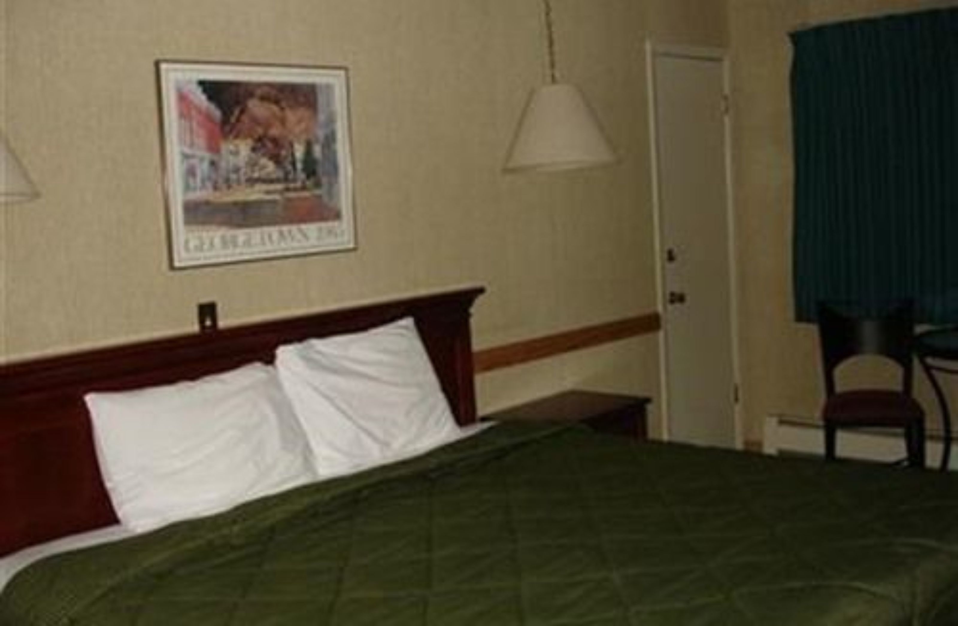 A hotel room with a bed, a framed picture on the wall, a chair, and a door.