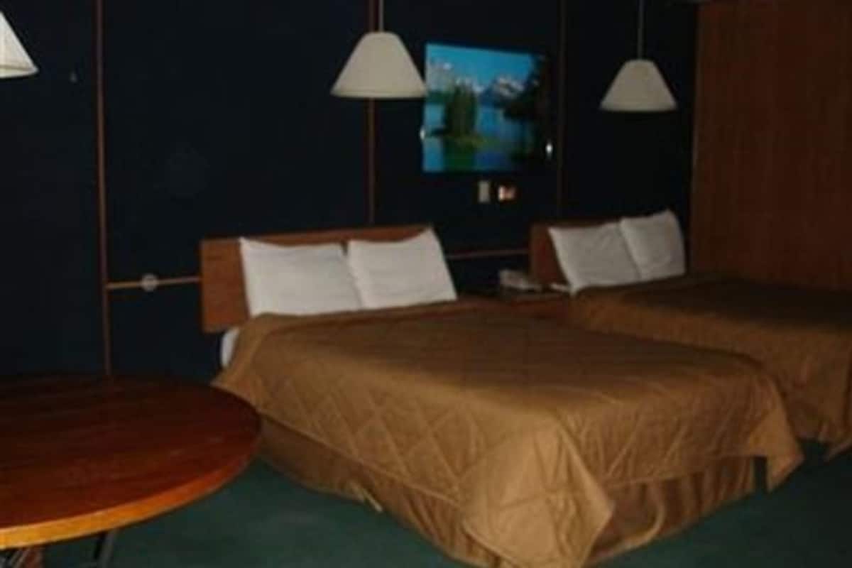 Quarto de hotel com duas camas, uma mesa redonda e televisão na parede.