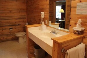 A wooden cabin-style bathroom with a white sink, a mirror, and a toilet.