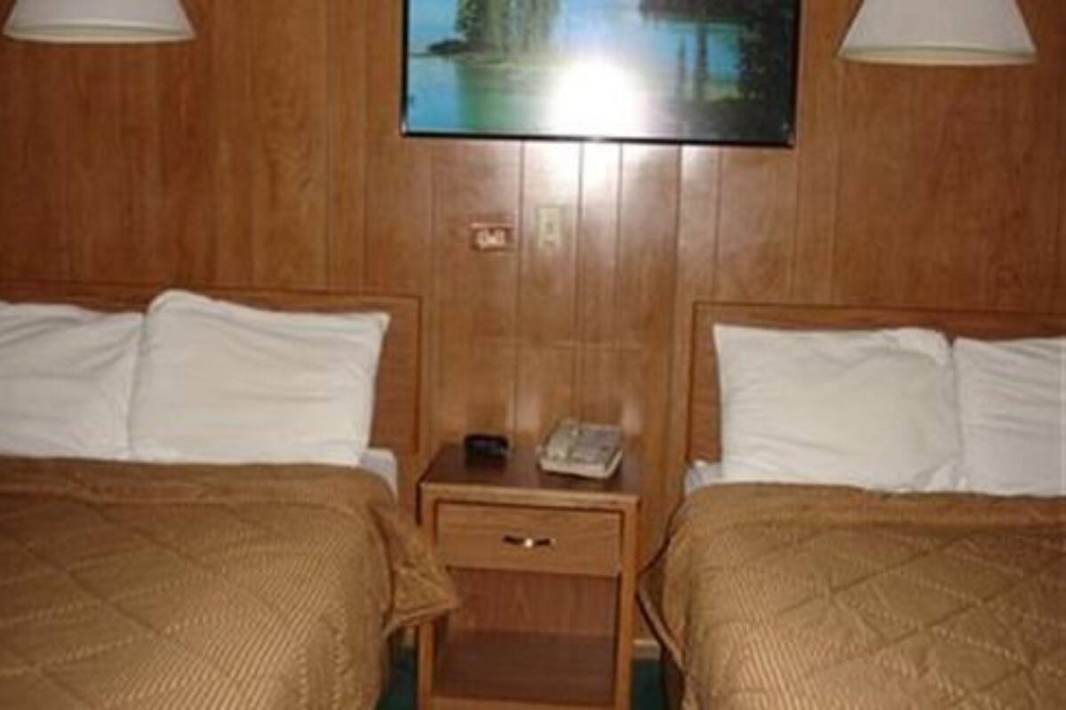 Quarto de hotel com duas camas, painéis de madeira, mesa de cabeceira com telefone e um quadro na parede.