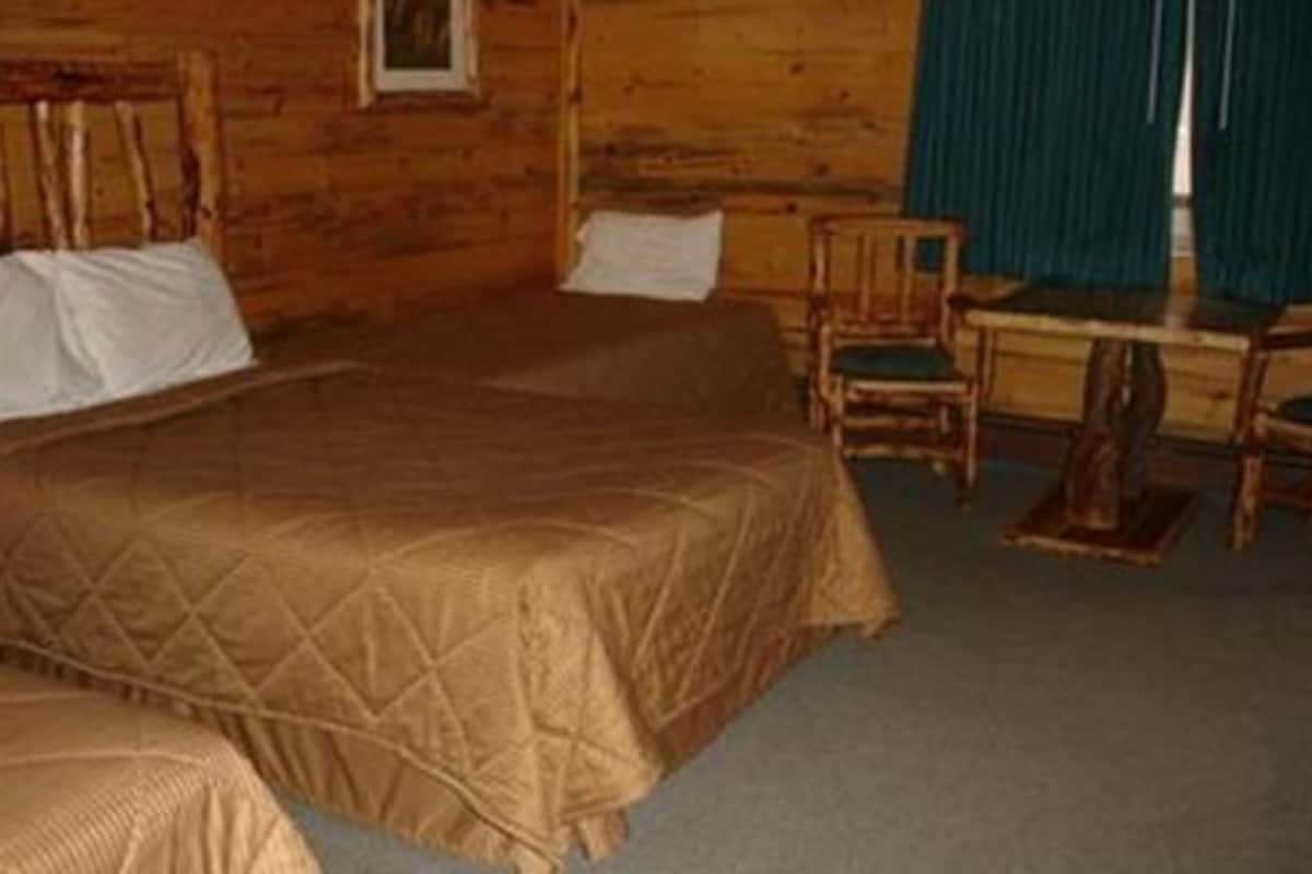 Quarto de cabana de madeira com duas camas, uma escrivaninha e uma cadeira.