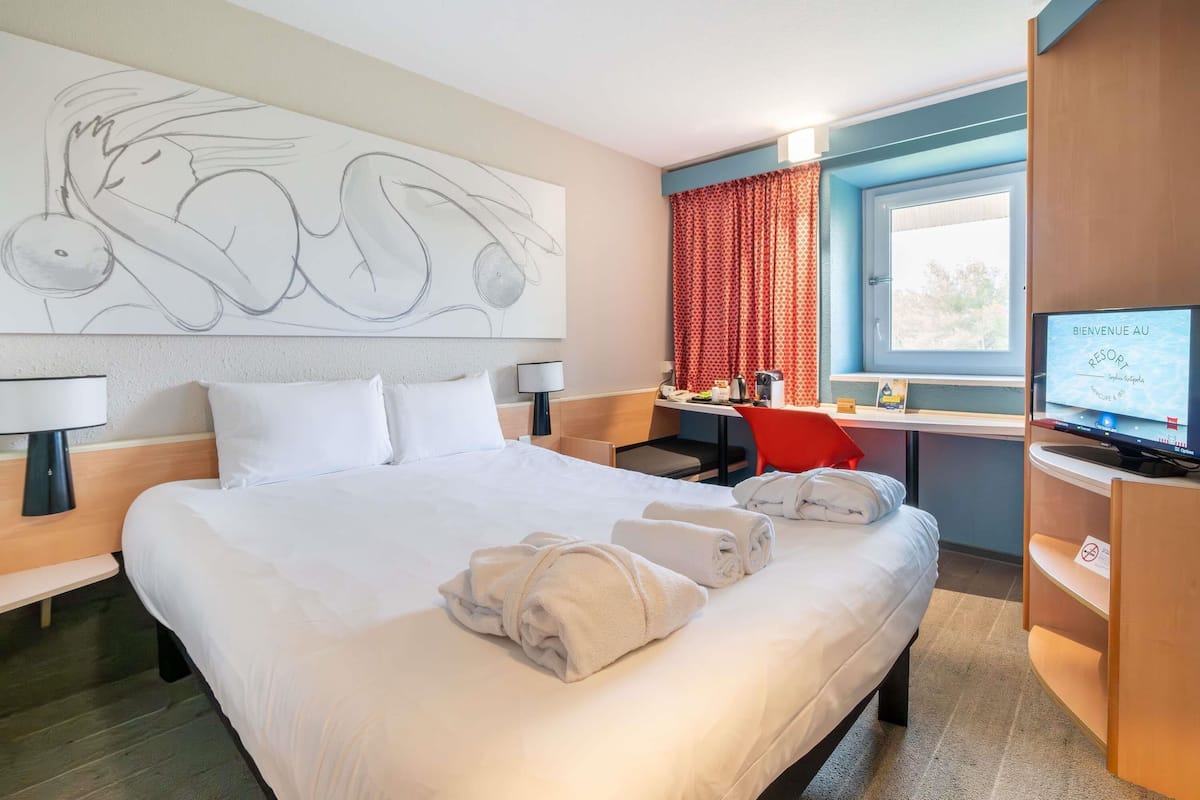 Une chambre dâhĂŽtel avec un grand lit, un bureau, une tĂ©lĂ©vision et une fenĂȘtre avec des rideaux.