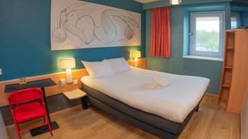 Hotelkamer met een groot bed, een bureau, een stoel, een raam met gordijnen en een kunstwerk aan de muur.
