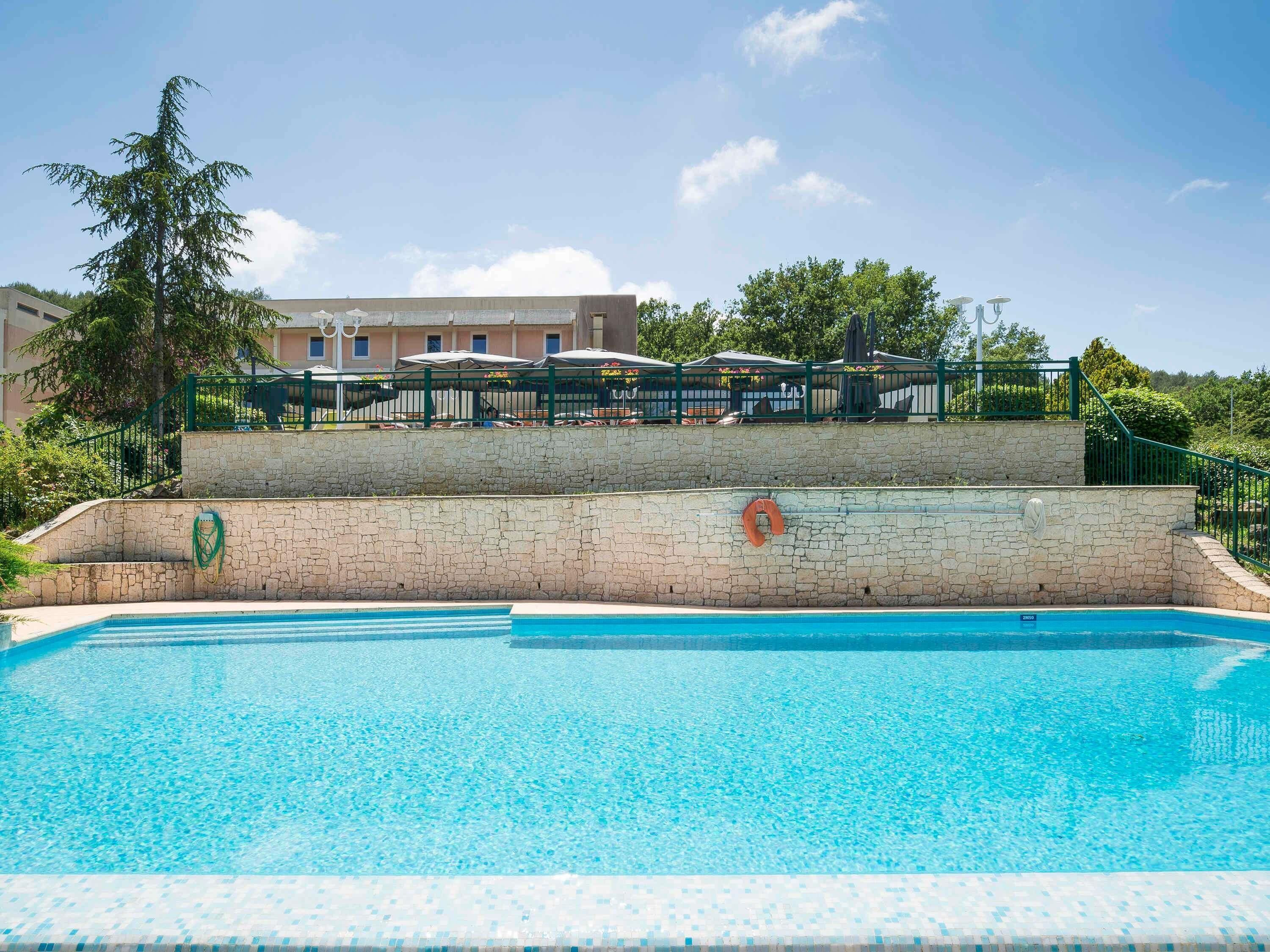 A swimming pool with a stone wall, a lifebuoy, and a green fence.