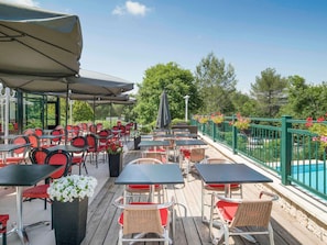 An outdoor patio with tables and chairs, a pool, and a green fence.