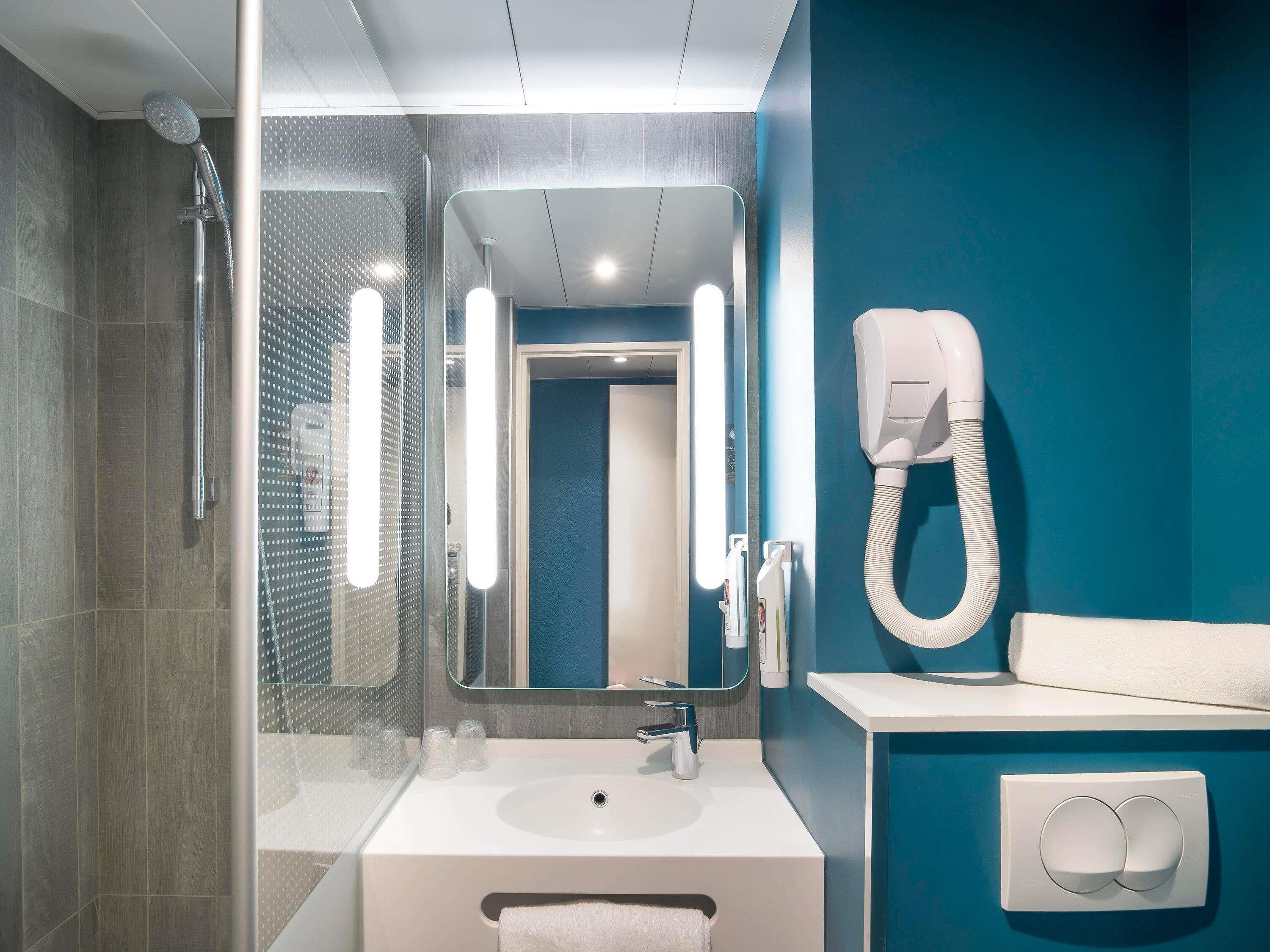 Une salle de bain moderne avec une douche à parois de verre, un lavabo blanc, un miroir et un porte-serviettes.
