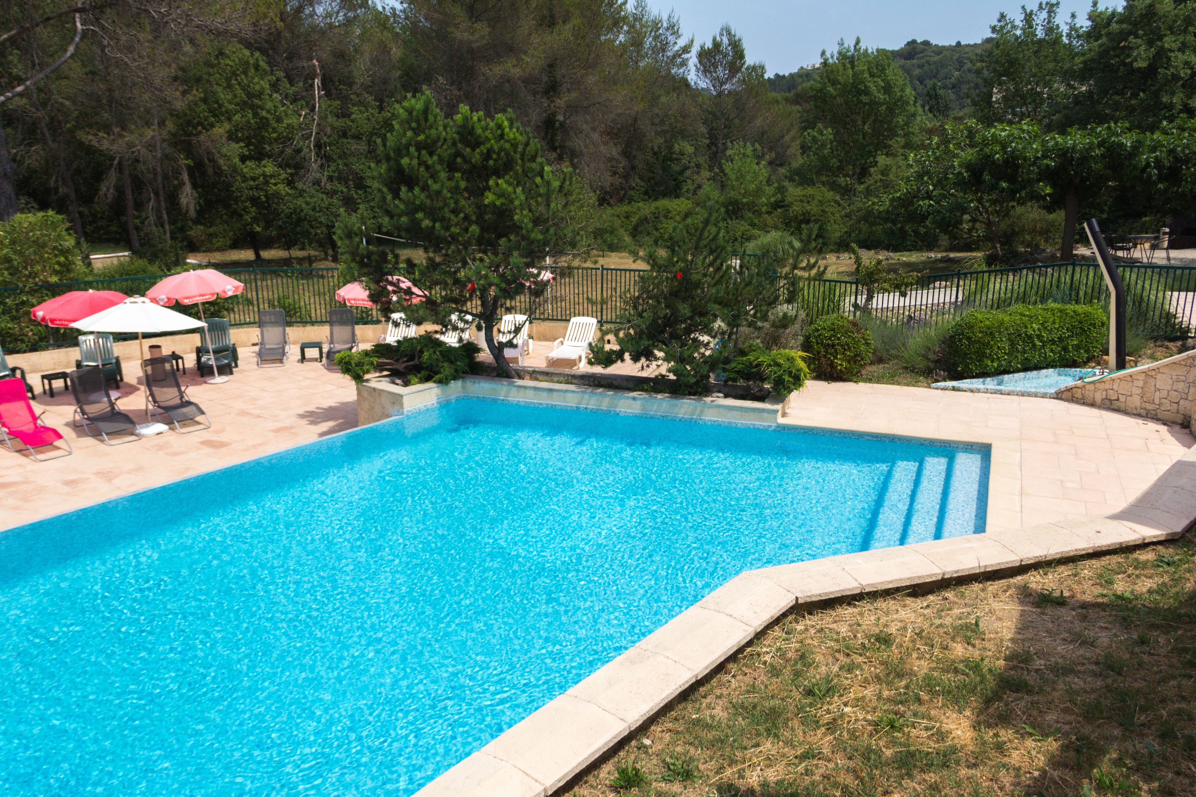 A rectangular swimming pool with a tiled edge, surrounded by a grassy area with several lounge chairs and umbrellas.
