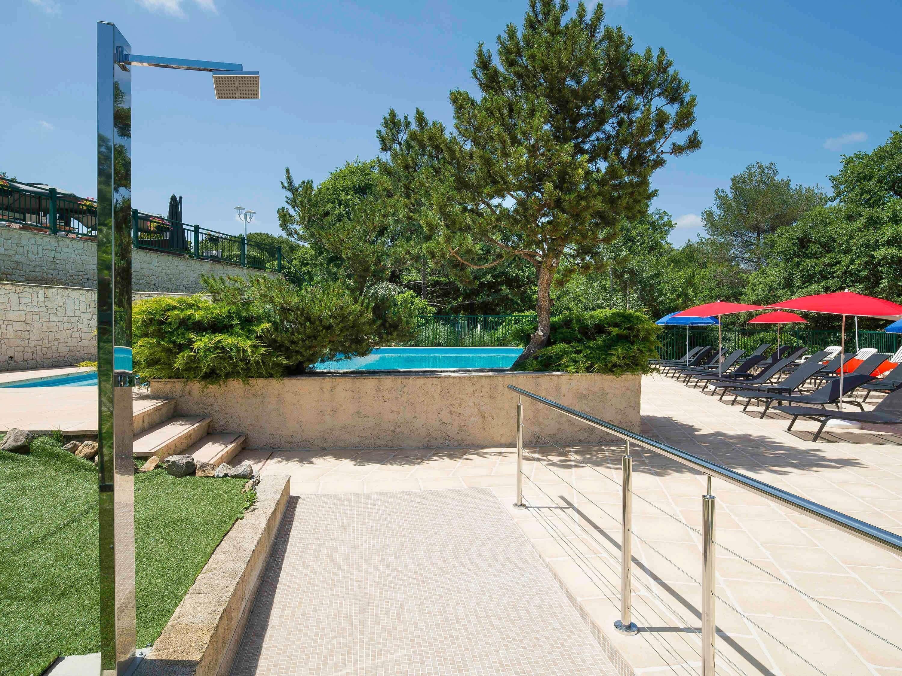 Area piscina con poltronne a sdraio e ombrelloni, una parete in pietra e una ringhiera in metallo.