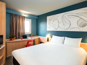 Een hotelkamer met een bed, bureau, televisie en een groot abstract schilderij aan de muur.