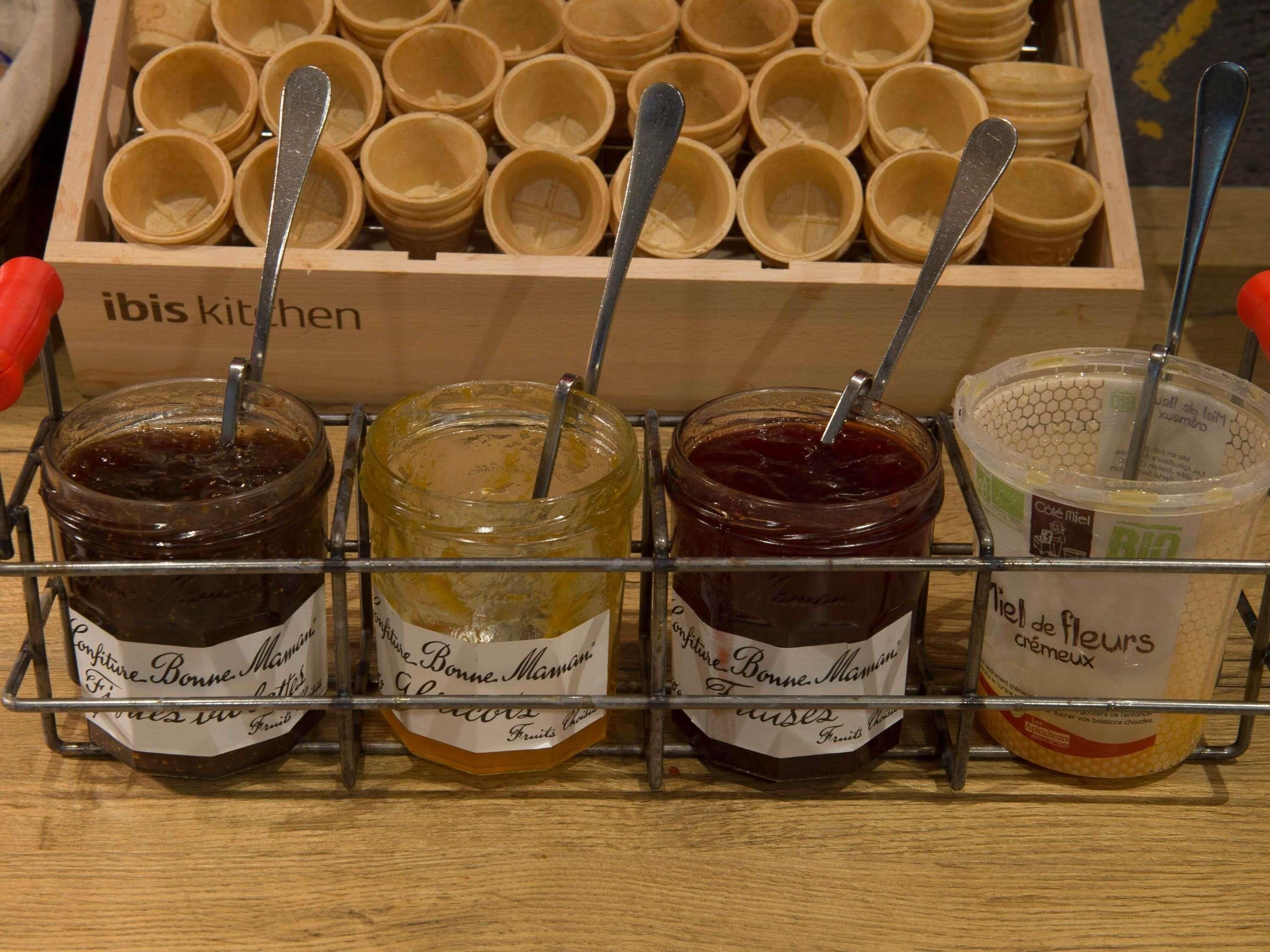 Eine Auswahl an Lebensmitteln, darunter Gläser mit Marmelade und ein Behälter mit Honig, jeweils mit einem Löffel.