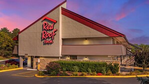 Um Red Roof Inn com uma placa grande nas cores vermelha e preta, fachada de pedra e estacionamento com vagas demarcadas em amarelo.