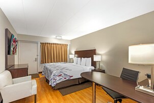 Habitación de hotel con cama, mesitas de noche, escritorio, silla, lámpara y televisor en la pared.
