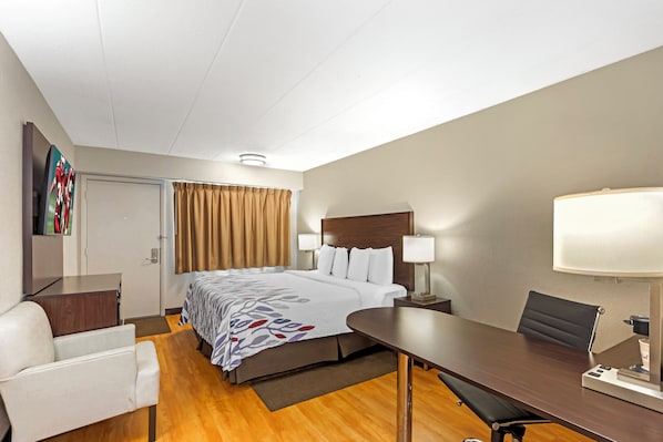 A hotel room with a bed, bedside tables, a desk, a chair, a lamp, and a TV on the wall.