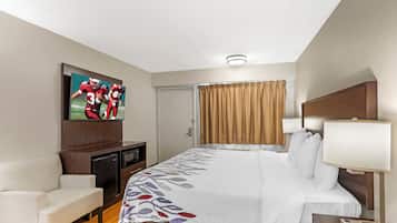 Habitación de hotel con cama, televisión montada en la pared, escritorio con lámpara, una silla y una puerta.