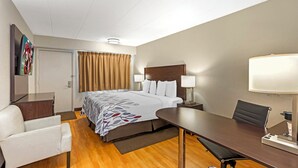 Quarto de hotel com cama, mesas de cabeceira, escrivaninha, cadeira, luminária e televisão na parede.